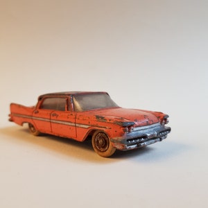 May include: A vintage toy car model of a red sedan with a black roof and chrome accents. The car has a weathered, worn look, suggesting it is an antique.