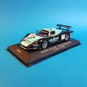 May include: A black and blue 1:18 scale model of a Maserati MC12 race car with the number 10 and the words "vitaphone" on the side. The car is on a black display base with the text "MASERATI MC12 #10 FIA GT 2nd Monza 2005 F. Babini - T. Biagi" printed on it.