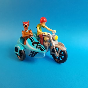 May include: A blue and silver toy motorcycle with a sidecar. The motorcycle has a skull and crossbones design on the sidecar. A cartoon character is riding the motorcycle and another cartoon character is sitting in the sidecar.