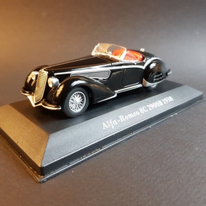 May include: A black 1938 Alfa-Romeo 8C 2900B model car on a black display base. The car has a red interior and chrome accents.