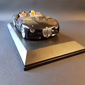 May include: A black and yellow model car on a black display stand. The car has a sleek, futuristic design with a large grille and a low profile.