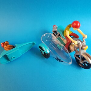 May include: A blue and silver toy motorcycle with a clear sidecar. A cartoon character with a red hat is riding the motorcycle. A separate blue sidecar with a cartoon dog figure is included.