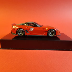 May include: A red Ferrari 430 Scuderia race car model with a black base and the number "3" on the side.