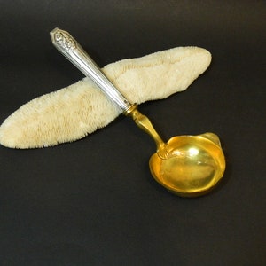 May include: A silver and gold ladle with an ornate handle. The ladle is resting on a piece of white coral.
