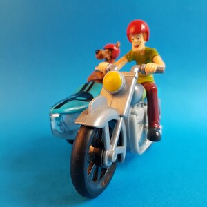 May include: A silver and blue toy motorcycle with a sidecar. A cartoon character wearing a red helmet is driving the motorcycle. A cartoon dog wearing a red helmet is in the sidecar.