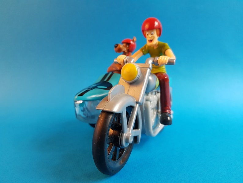 May include: A silver and blue toy motorcycle with a sidecar. A cartoon character wearing a red helmet is driving the motorcycle. A cartoon dog wearing a red helmet is in the sidecar.
