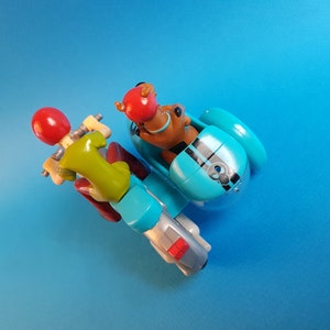 May include: A blue and silver toy motorcycle with a sidecar. A green and red figure is driving the motorcycle and a brown figure is in the sidecar.