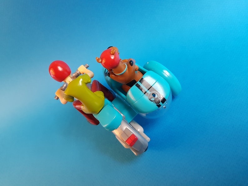 May include: A blue and silver toy motorcycle with a sidecar. A green and red figure is driving the motorcycle and a brown figure is in the sidecar.