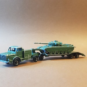 May include: A green toy truck hauling a green toy tank on a flatbed trailer.