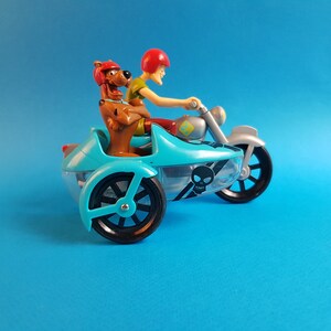 May include: A blue and silver toy motorcycle with a sidecar. A brown dog and a red-haired person are riding the motorcycle. The sidecar has a skull and crossbones design.