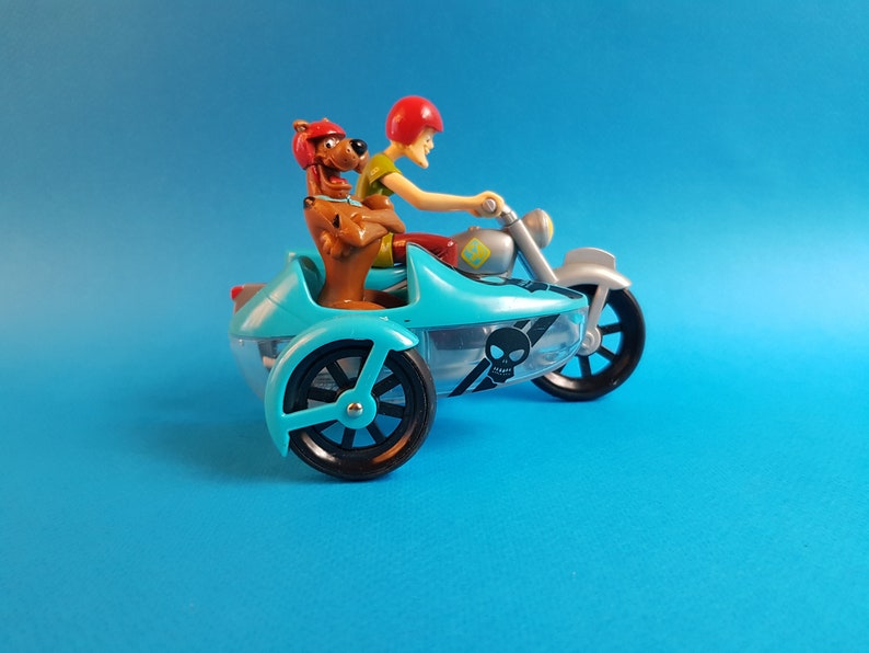 May include: A blue and silver toy motorcycle with a sidecar. A brown dog and a red-haired person are riding the motorcycle. The sidecar has a skull and crossbones design.