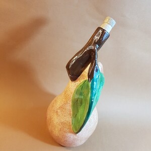 May include: A ceramic pear-shaped bottle with a dark brown spout and a cork stopper. The pear is tan with a green leaf. The bottle is a decorative item.