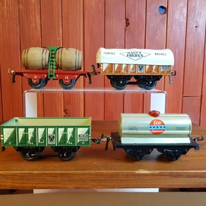 May include: Four vintage toy train cars. One red car carries two wooden barrels. Another has a white top with text. A green car has a geometric design, and a silver car has a red top and the text "Eco Essence".