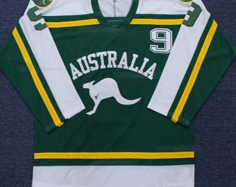 Puede incluir: Una camiseta de hockey verde y blanca con la palabra "AUSTRALIA" y un logotipo de canguro en la parte delantera. El número "9" está en el hombro derecho y el número "5" está en el hombro izquierdo.