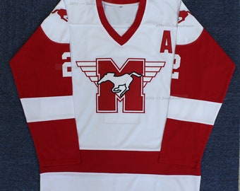 Puede incluir: Jersey de hockey blanco con rayas rojas y blancas. El jersey tiene una "M" roja con un caballo blanco y alas en la parte delantera. El número "2" está en la manga derecha y una "A" roja está en la manga izquierda.