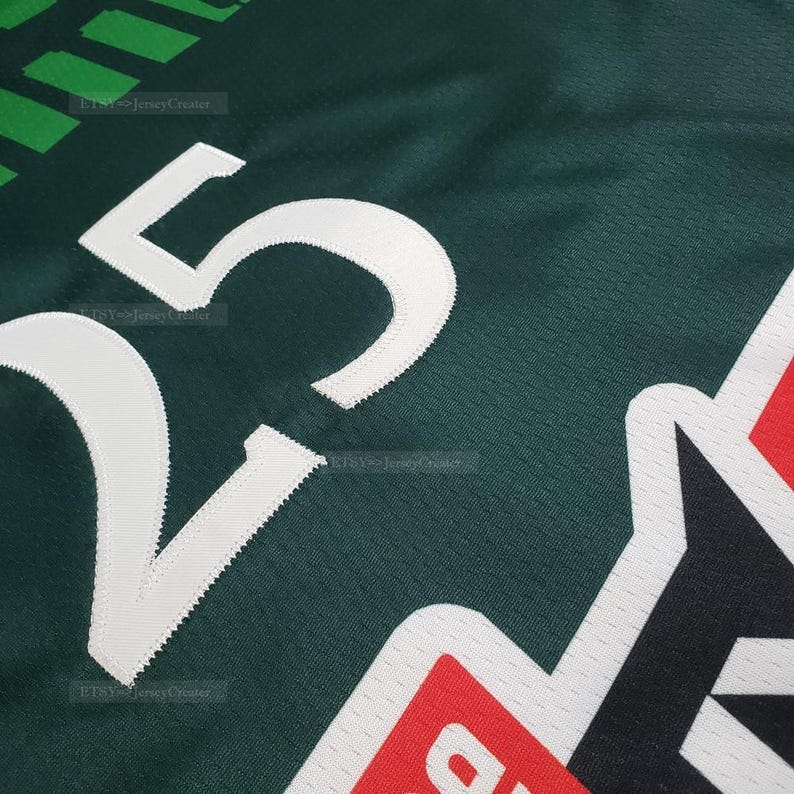 Puede incluir: Primer plano de una camiseta verde oscuro con el n&uacute;mero "25" en blanco. La camiseta tiene un dise&ntilde;o en forma de estrella roja, negra y blanca en el lado derecho. La tela tiene una apariencia texturizada.