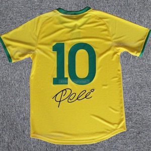 May include: A yellow soccer jersey with green trim on the collar and sleeves. The number "10" is printed in green on the back, along with the name "Pele" in a black script font. The jersey is made of a lightweight material.