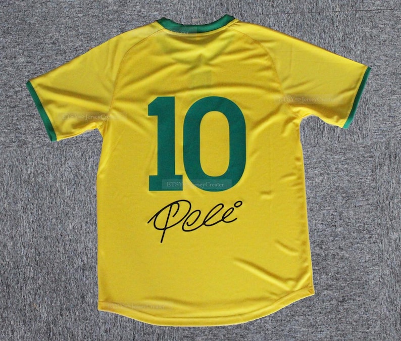 May include: A yellow soccer jersey with green trim on the collar and sleeves. The number "10" is printed in green on the back, along with the name "Pele" in a black script font. The jersey is made of a lightweight material.