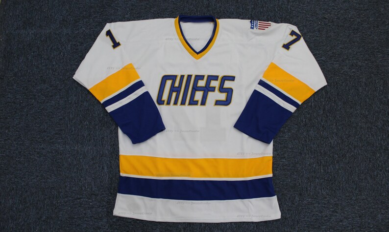 May include: White hockey jersey with blue and gold stripes. The jersey has the word "CHIEFS" in blue on the front and the numbers "1" and "7" on the sleeves.