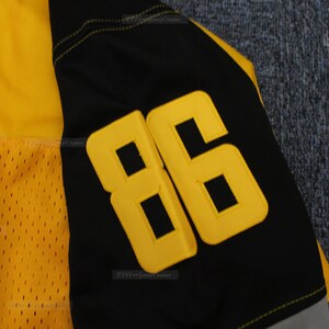 May include: Close-up of a black and yellow football jersey with the number "86" stitched on the sleeve.
