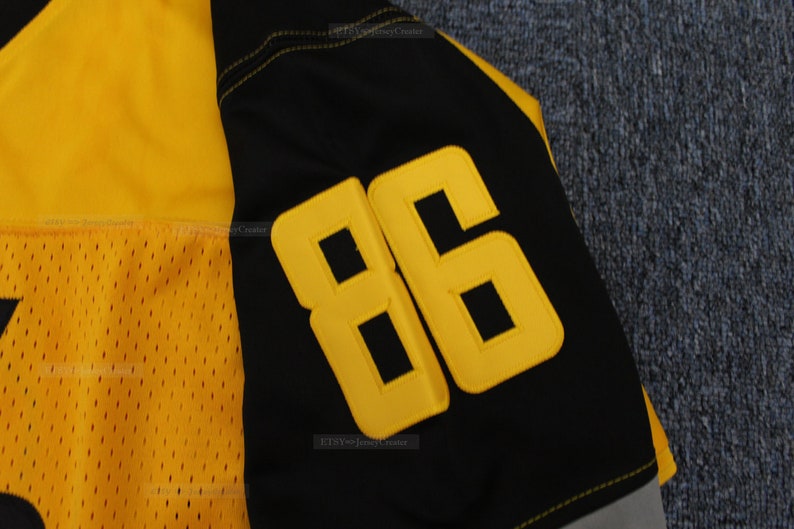 May include: Close-up of a black and yellow football jersey with the number "86" stitched on the sleeve.