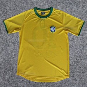 May include: A yellow short-sleeved jersey with green trim on the collar and sleeves. The jersey features a crest on the chest with blue, green, and white details. The jersey is made of a lightweight material.