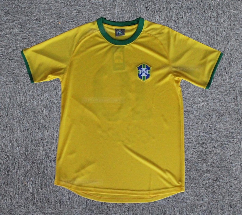 May include: A yellow short-sleeved jersey with green trim on the collar and sleeves. The jersey features a crest on the chest with blue, green, and white details. The jersey is made of a lightweight material.