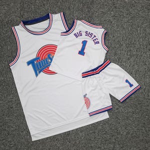 Könnte beinhalten: Weißes Basketball-Trikot und Shorts-Set. Das Trikot zeigt das Looney Tunes-Logo und den Text. Die Shorts und das Trikot haben blaue und rote Verzierungen. Das Trikot hat die Nummer 1 und die Worte "Big Sister".