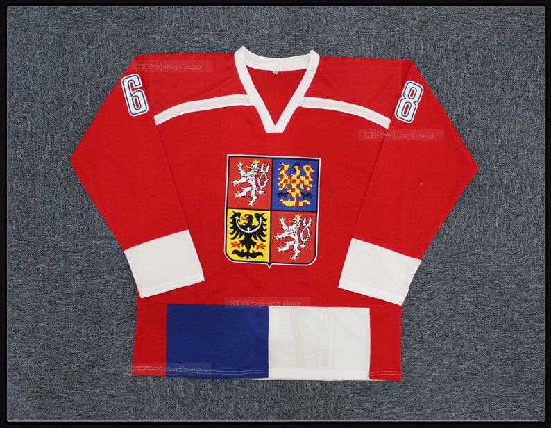 Peut inclure: Maillot de hockey rouge avec des d&eacute;tails blancs et bleus. Le maillot pr&eacute;sente un col en V, des poignets blancs et les num&eacute;ros 6 et 8 sur les manches. Un &eacute;cusson avec des armoiries est centr&eacute; sur la poitrine.