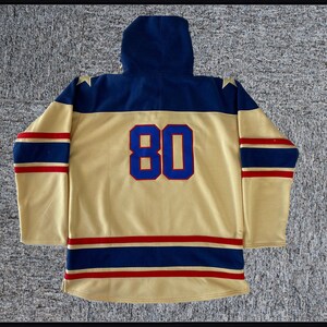 May include: A gold hockey jersey with blue and red stripes. The jersey has a navy blue hood and the number "80" on the back.