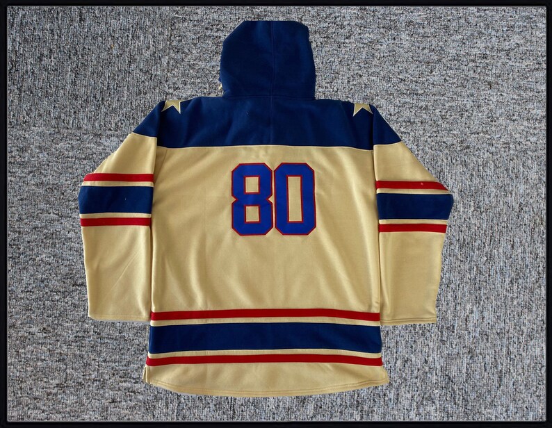 May include: A gold hockey jersey with blue and red stripes. The jersey has a navy blue hood and the number "80" on the back.