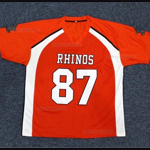 May include: Red and white football jersey with black trim. The jersey has the word "RHINOS" and the number "87" on the front. The jersey has a small rhino logo on the sleeves.