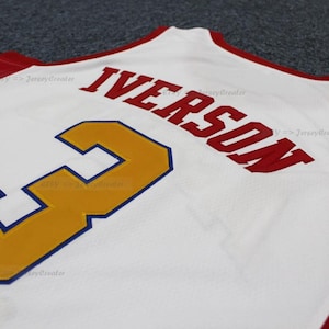 May include: White basketball jersey with red trim and the name "IVERSON" in red block letters. The number "3" is in gold with a blue outline. The jersey is made of a breathable fabric.