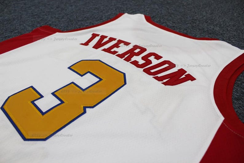 May include: White basketball jersey with red trim and the name "IVERSON" in red block letters. The number "3" is in gold with a blue outline. The jersey is made of a breathable fabric.