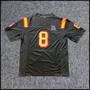 May include: A black short-sleeved jersey with a V-neck collar. The front features a large yellow and red number 8 and a small logo with the text LUTHONCOMB. The shoulders have yellow and red stripes, and the sleeves display the number 8.