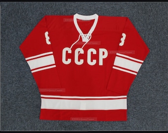 May include: A red hockey jersey with white stripes and the word "CCCP" in white letters on the front. The number "3" is on each sleeve.
