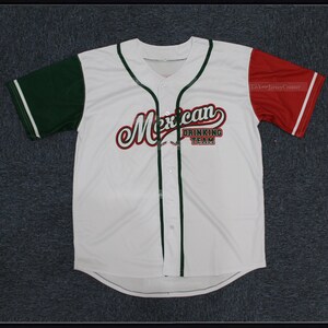 Pode incluir: Camisola de beisebol branca com mangas verdes e vermelhas. A camisola tem uma faixa verde e branca na frente e uma faixa verde e branca nas costas. A camisola tem o texto "Mexican Drinking Team" em uma fonte vermelha, branca e verde.