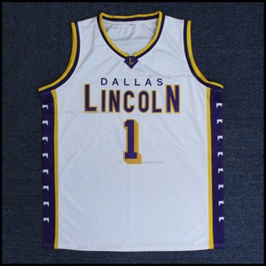 以下が含まれることがあります： 白のバスケットボールジャージ。紫と金のアクセント。ジャージには「DALLAS LINCOLN」の文字と数字の「1」が金色で表示されています。Vネックで小さな「L」のロゴが付いています。