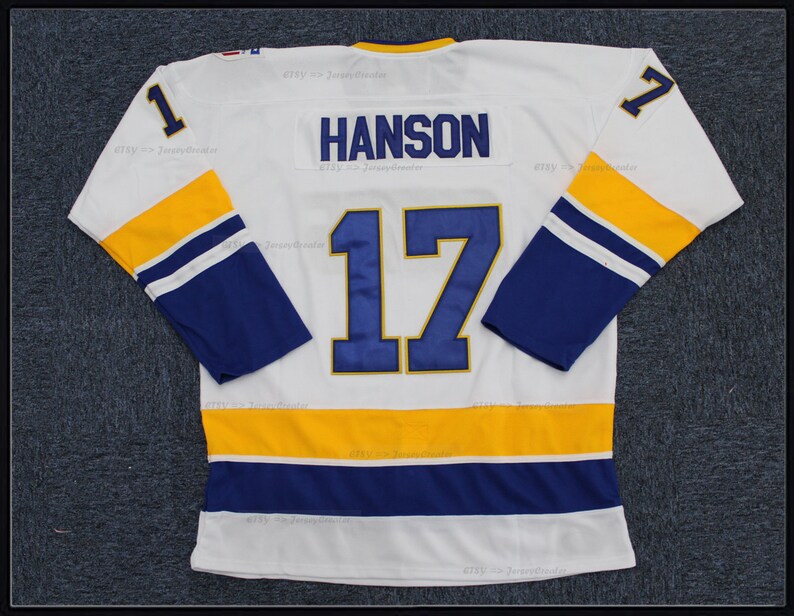 May include: White hockey jersey with blue and gold stripes. The number 17 is on the back with the name "HANSON" above it. The number 1 is on both sleeves.