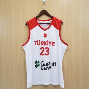 K&ouml;nnte beinhalten: Ein wei&szlig;es und rotes Basketballtrikot mit dem Wort "T&Uuml;RKIYE" in Rot, der Nummer "23" und dem Logo "Garanti BBVA". Das Trikot hat einen V-Ausschnitt und ist &auml;rmellos.
