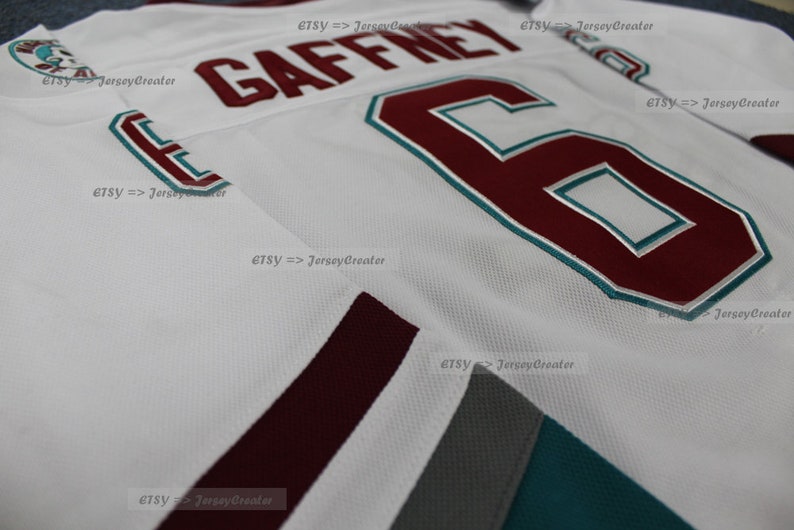 May include: White hockey jersey with maroon and teal accents. The number "6" and the name "GAFFNEY" are printed on the front of the jersey in maroon.