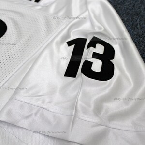K&ouml;nnte beinhalten: Wei&szlig;es Fu&szlig;balltrikot mit schwarzen Nummern "13" auf dem &Auml;rmel. Das Trikot ist aus Netzmaterial und hat einen wei&szlig;en Hintergrund.