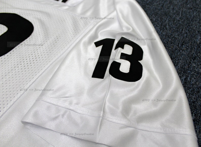 K&ouml;nnte beinhalten: Wei&szlig;es Fu&szlig;balltrikot mit schwarzen Nummern "13" auf dem &Auml;rmel. Das Trikot ist aus Netzmaterial und hat einen wei&szlig;en Hintergrund.