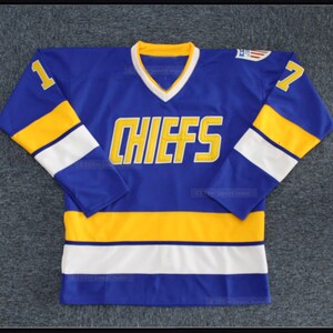 May include: A blue hockey jersey with yellow and white stripes. The jersey has the word "CHIEFS" in yellow lettering on the front and the number "1" on the left sleeve and the number "7" on the right sleeve.