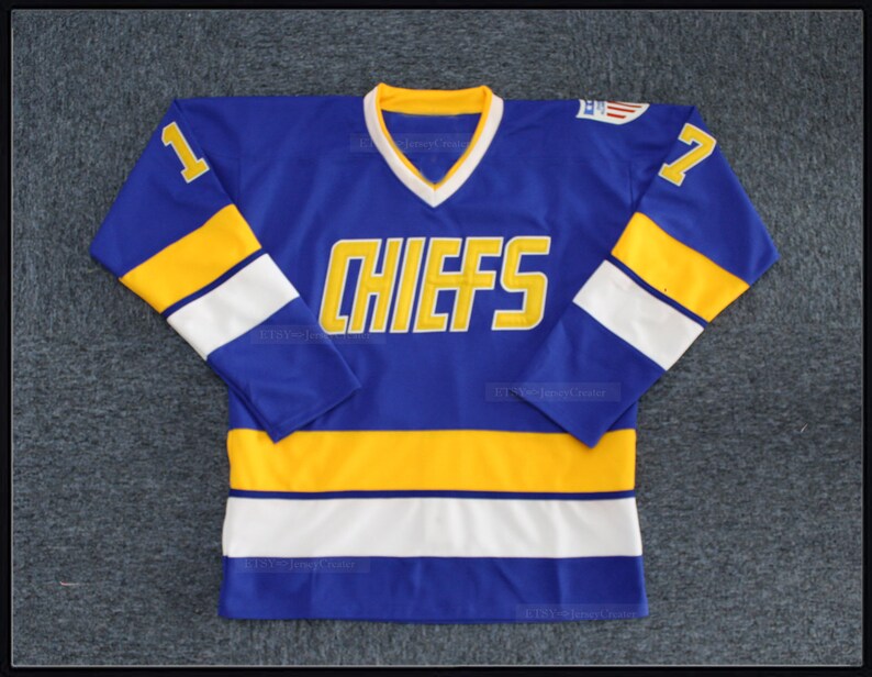 May include: A blue hockey jersey with yellow and white stripes. The jersey has the word "CHIEFS" in yellow lettering on the front and the number "1" on the left sleeve and the number "7" on the right sleeve.