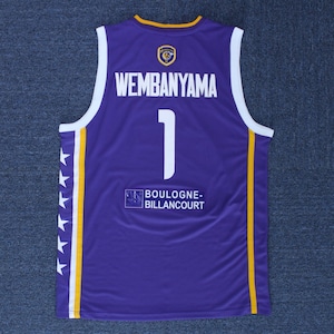 May include: Purple basketball jersey with white and yellow accents. The back of the jersey has the name "Wembanyama" and the number "1" in white. The text "BOULOGNE-BILLANCOURT" is printed below the number.