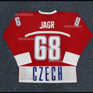 Peut inclure: Un maillot de hockey rouge avec des d&eacute;tails blancs et bleus. Le maillot affiche le nom "JAGR" au-dessus du num&eacute;ro "68" en blanc, avec le mot "CZECH" en bas. Le num&eacute;ro "6" est sur la manche gauche et "8" sur la droite.