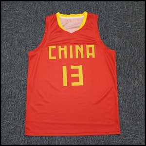 May include: Red basketball jersey with yellow lettering that says "CHINA" and the number "13".