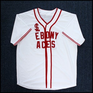 May include: White baseball jersey with red trim and the words "Ebony Aces" in red lettering.