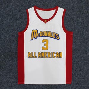 May include: White basketball jersey with red accents and the McDonald's logo. The jersey features the number 3 in gold and the words "ALL AMERICAN" in gold lettering.